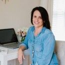 a woman sitting at a white desk with a laptop on it and flowers in front of her