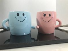 two coffee mugs with faces drawn on them are sitting on a counter next to each other