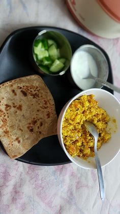 a black plate topped with food next to a bowl of salad and pita bread