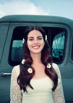 a woman standing in front of a green truck with flowers in her hair and smiling at the camera