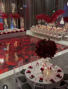 a table set up for an event with red flowers and candles in the center, surrounded by white chairs