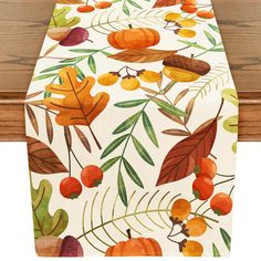 an image of a table runner with autumn leaves and berries on white fabric, along with wood planks