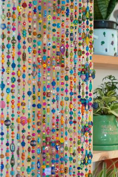 beads hanging from the side of a curtain in front of a potted plant on a shelf