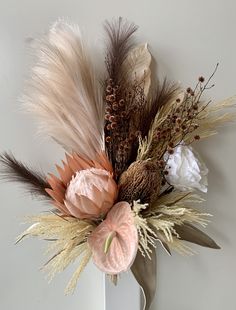 a vase filled with flowers and feathers on top of a white table next to a wall