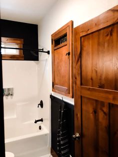 a bathroom with wooden cabinets and white bathtub next to a black towel rack on the wall