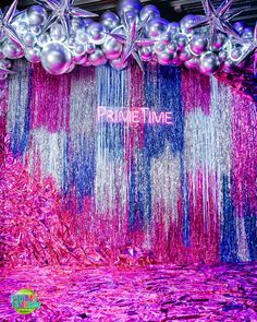 purple and silver balloons are hanging from the ceiling in front of a backdrop with streamers