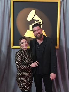 a man and woman standing next to each other in front of a wall with an award on it