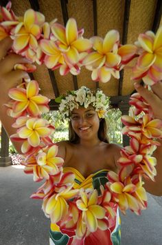 a woman in a hawaiian dress holding flowers up to her face and smiling at the camera