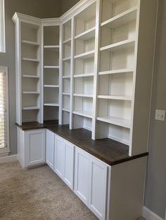 an empty room with white bookcases and brown counter top in the middle, along with carpeted flooring