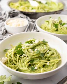 two white bowls filled with guacamole and garnished with cilantro