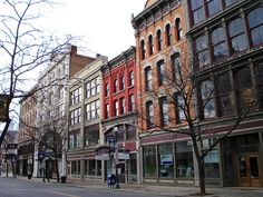 several buildings line the street in front of a man walking down the sidewalk with his bicycle