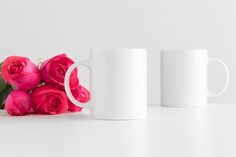 two white coffee mugs with pink roses next to each other on a white surface