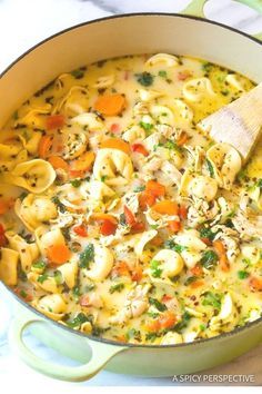 a pot filled with pasta and vegetables on top of a table next to a wooden spoon