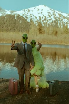 two people dressed in alien costumes standing next to each other near a body of water