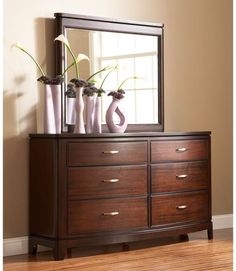 a dresser with flowers and vases on it in front of a large framed mirror