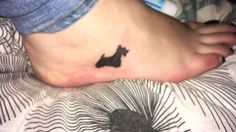 a person with a small black dog tattoo on their foot is laying down in bed