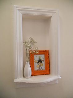 an orange and white vase sitting on top of a shelf next to a framed picture