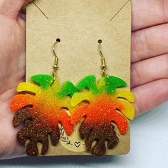 a pair of handmade earrings with orange, yellow and green flowers on them in front of a card