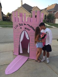 a man and woman standing in front of a pink castle with writing on the door