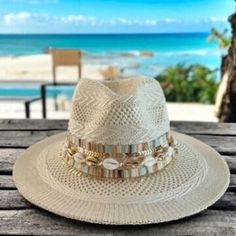 Calling all beach babes and summer queens!   Surf's up for the season with this on-trend panama hat, the perfect accessory to catch some rays and turn heads wherever you go.  This beauty features a classic cream-colored straw hat with a wide brim for maximum sun protection, accented with delicate seashells and gleaming gold chains for a touch of boho chic.  Whether you're strolling along the shoreline or sipping cocktails at a rooftop bar, this hat is sure to add a touch of whimsical flair to yo Chic Beach Hats For Sunbathing, Chic Sunbathing Hat For Beach Season, Chic Straw Hat For Beach, Summer Beachy Hats For Sunbathing, Beachy Summer Hats For Sunbathing, Brimmed Beachwear Hat For Sunbathing, Bohemian White Straw Fedora, White Bohemian Bucket Hat, Chic Beige Beach Hat