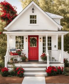 a small white house with red door and flowers on the front steps, surrounded by greenery