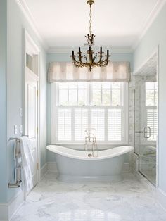 a white bath tub sitting under a chandelier in a bathroom next to a window