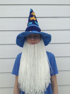 a young boy wearing a wizard hat with long white hair and blue shirt, standing in front of a house