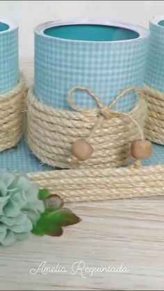 three blue cups with rope wrapped around them sitting on a table next to some flowers