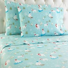 a bed topped with blue sheets and pillows covered in snowflakes, reindeers and trees