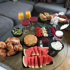 a glass table topped with plates of food and drinks next to a couch filled with fruit