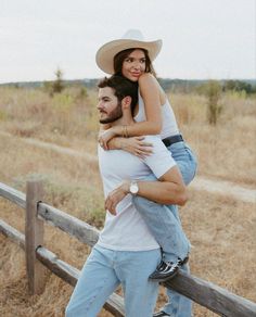 a man carrying a woman on his back while standing in front of a wooden fence