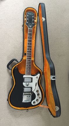 an electric guitar in its case on the floor next to it's carrying strap