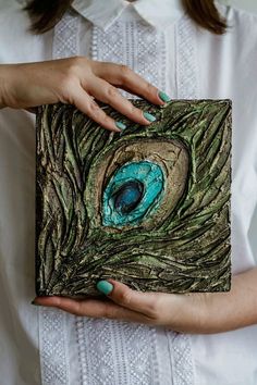 a woman holding a piece of art made out of tree branches with a peacock eye painted on it