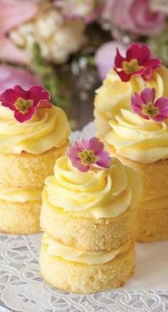 three small cupcakes with yellow frosting and pink flowers on top are sitting on a lace doily