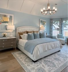 a bedroom with blue walls and white bedding, chandelier, dressers, and windows