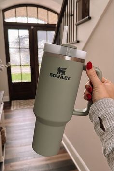 a woman holding a coffee cup in her hand while standing next to stairs with the name stanley on it