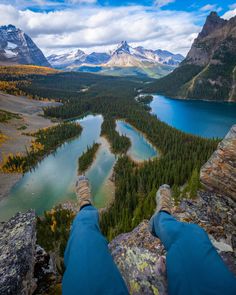 a person's feet hanging over the edge of a cliff overlooking a lake and mountains