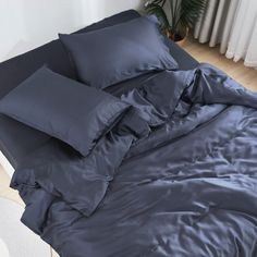 an unmade bed with grey sheets and pillows on it in a room that has wood floors