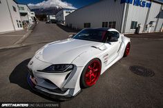 a white sports car is parked in front of a large building with red rims