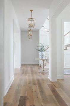 an empty hallway with white walls and wood flooring in the center, along with a chandelier hanging from the ceiling