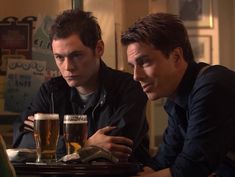 two men sitting at a table with beers in front of them