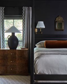 a bedroom with black walls and white bedding has a large vase on the dresser