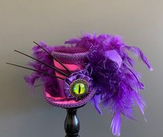 a purple top hat with feathers and a clock on the front is sitting on a stand