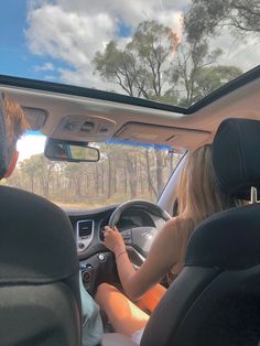 two people driving in the back seat of a car on a road with trees behind them