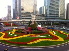 a large flower garden in the middle of a road with cars on it and tall buildings in the background