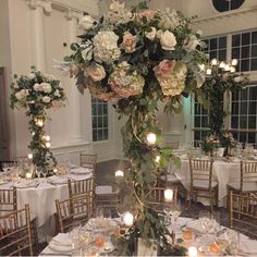 a tall vase filled with flowers sitting on top of a table covered in white linens