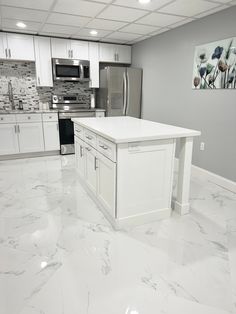 a kitchen with white cabinets and marble flooring in the middle of an empty room