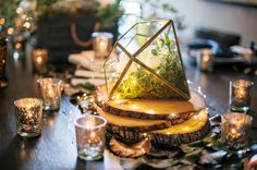 a wooden table topped with candles and a glass vase filled with plants on top of it