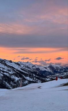 a person riding skis on top of a snow covered slope in the mountains at sunset