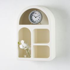 a white shelf with a clock and flower in it on the side of a wall